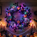 Halloween wreath with black eucalyptus, pumpkins, spiders, and LED lights, displayed with candles and skulls.
