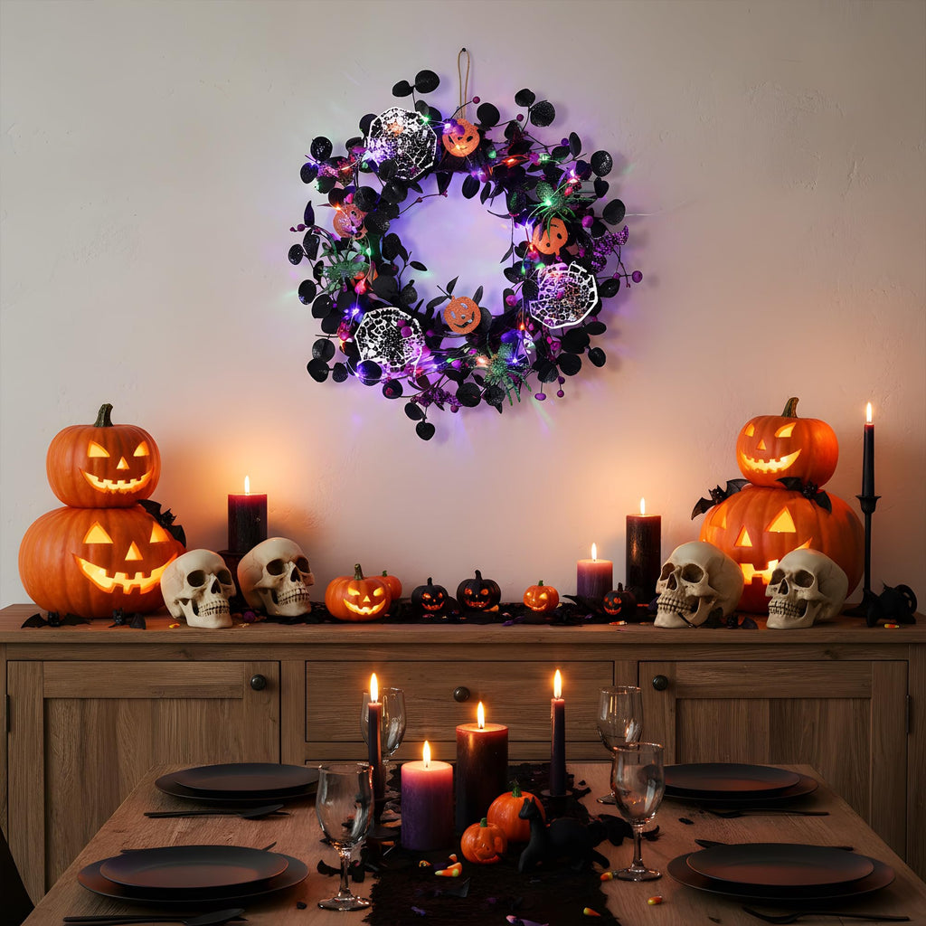 Halloween wreath with lights and decorations hanging above a table set for a spooky dinner with pumpkins and skulls