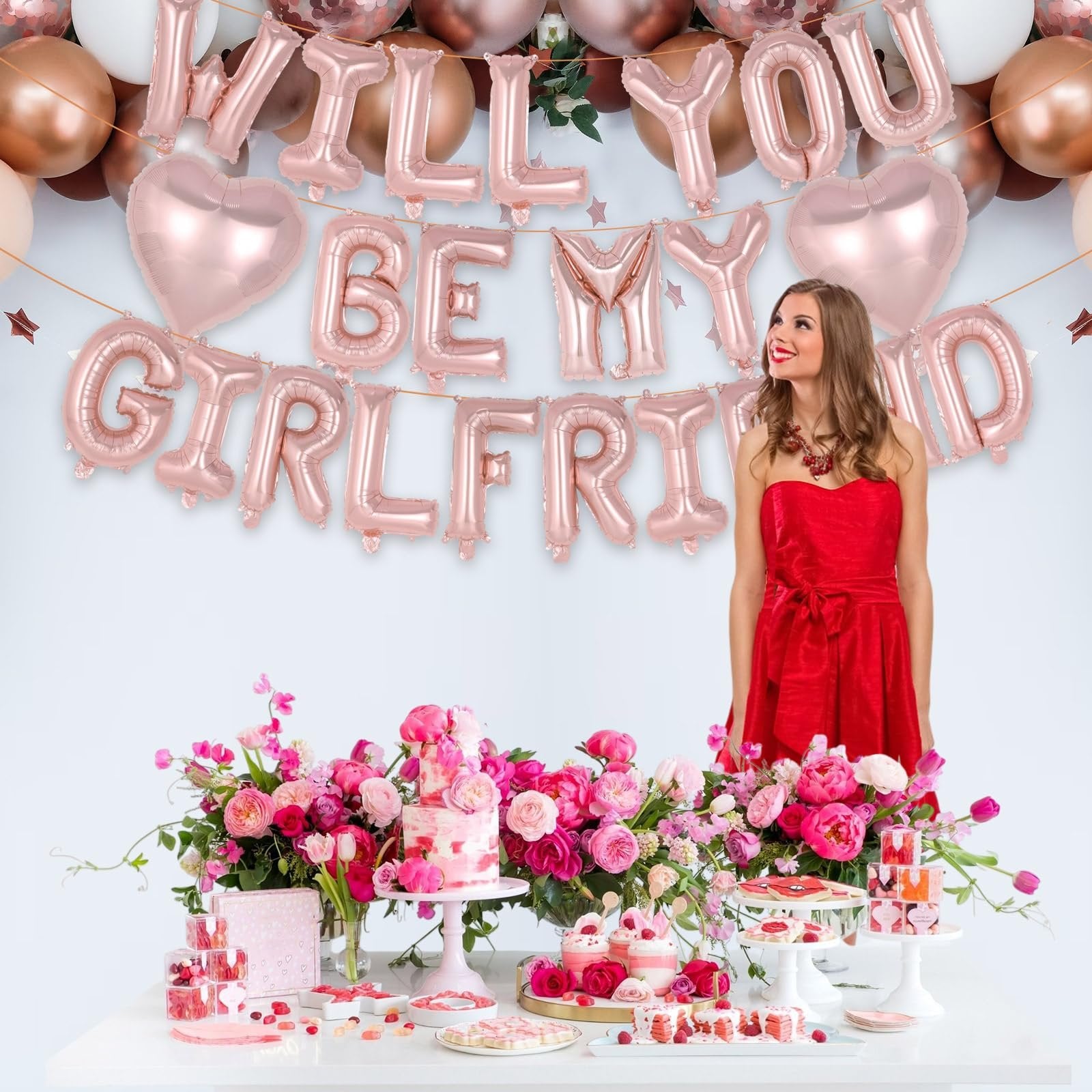 Rose gold foil balloons spelling 'Will You Be My Girlfriend' with a woman in a red dress and a table of desserts.