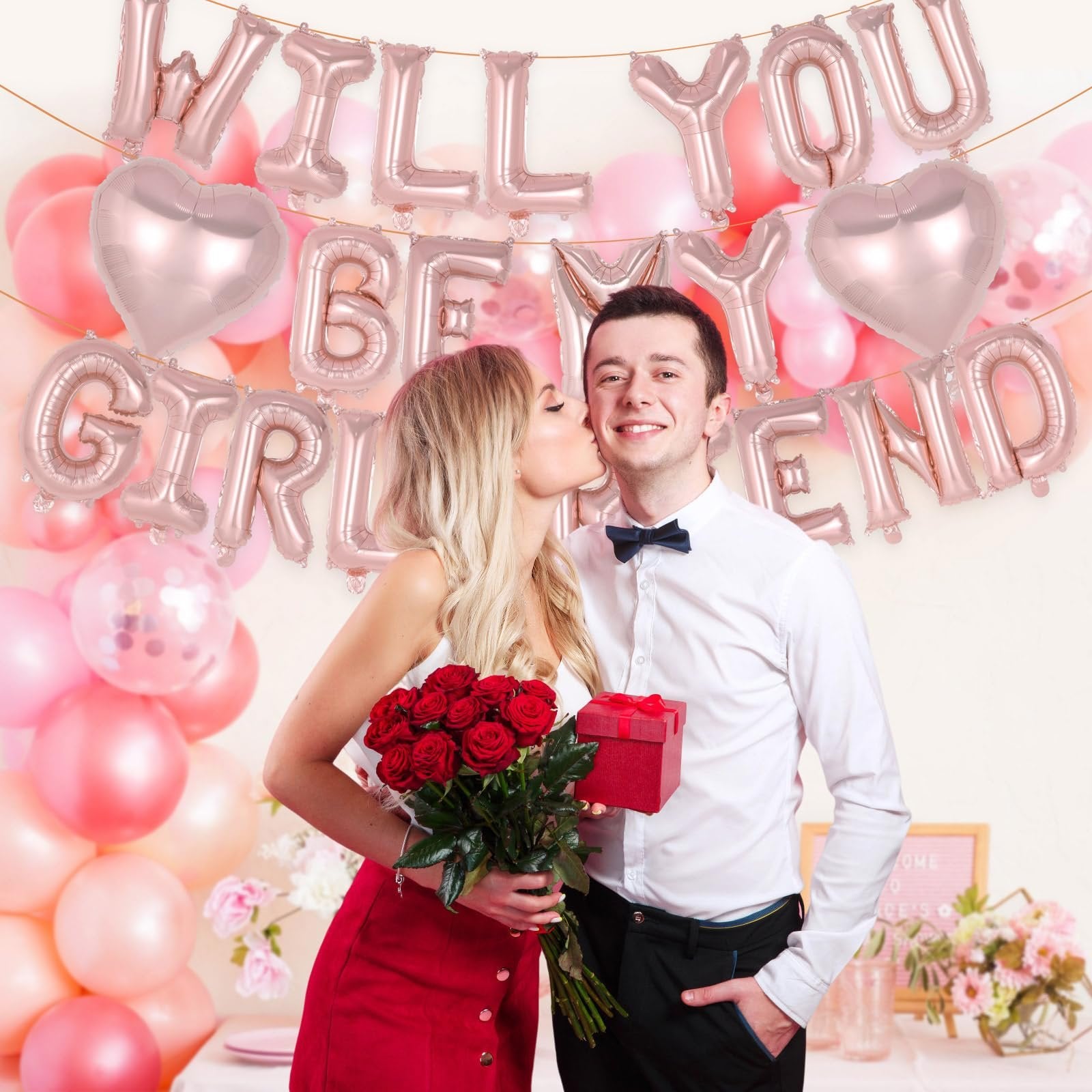 Couple celebrating proposal with rose gold 'Will You Be My Girlfriend' balloons and red roses