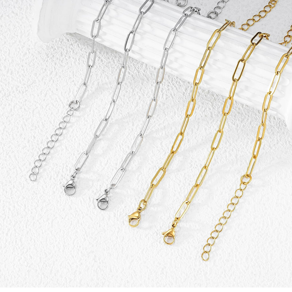 Gold and silver paperclip chains with lobster clasps and extension chains, laid out on a textured white surface.