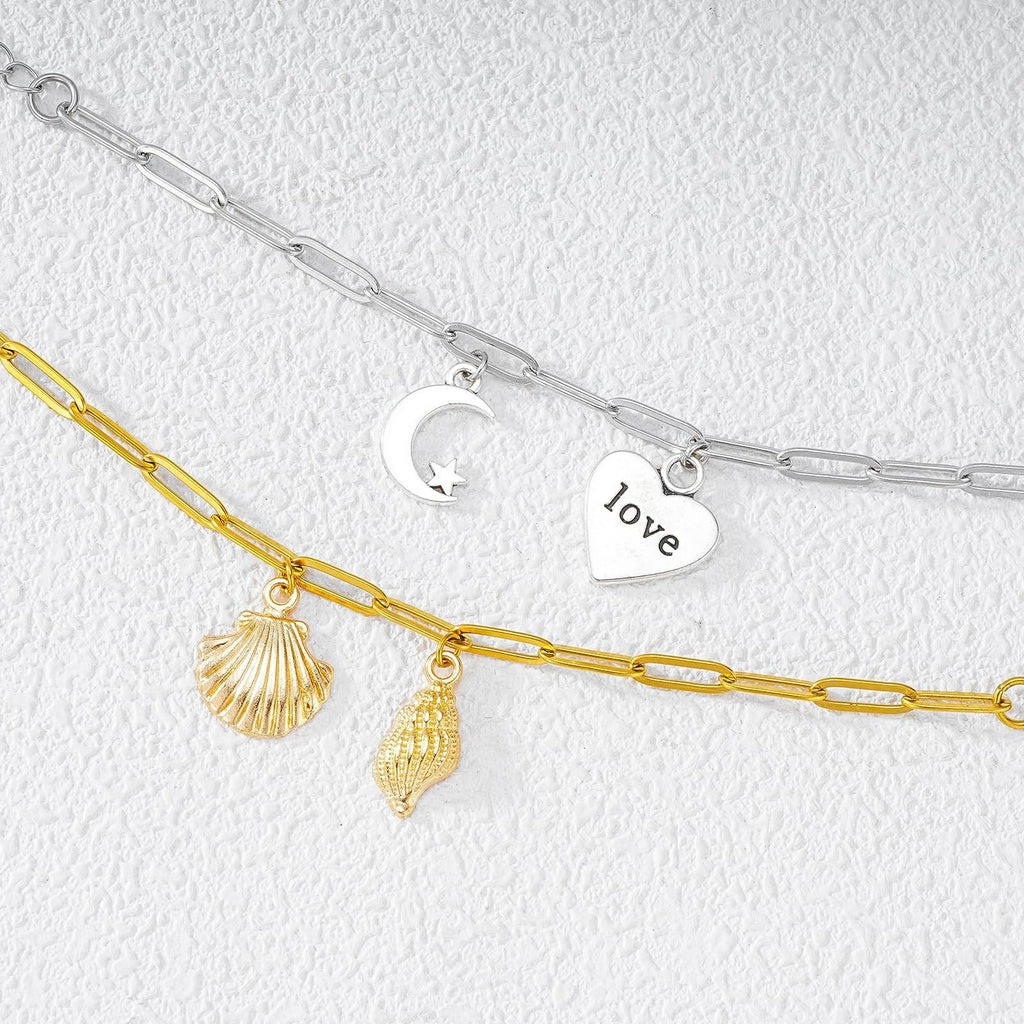 Gold and silver paperclip chains with charms including a seashell, conch shell, moon and star, and a heart with the word 'love'.
