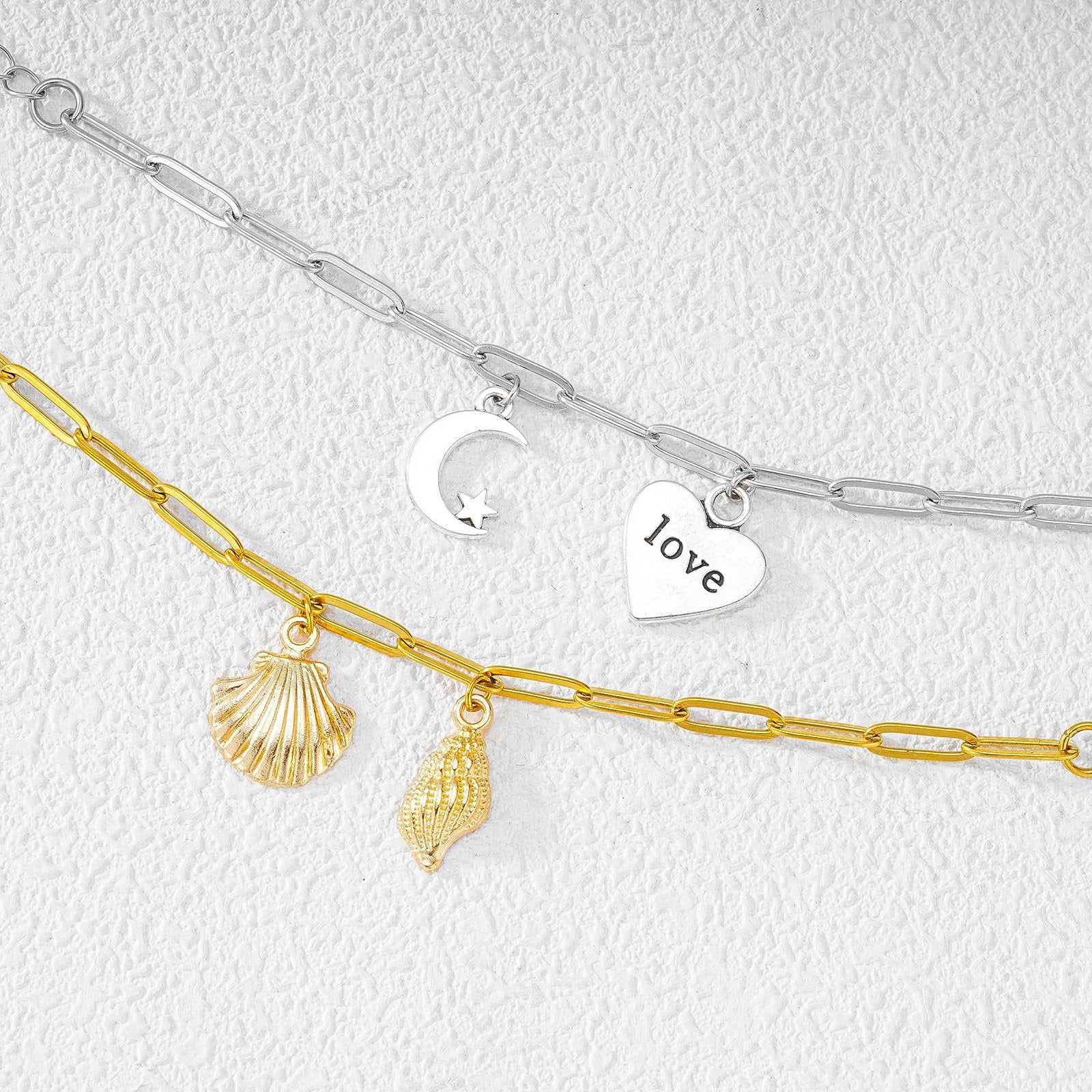 Gold and silver paperclip chains with charms including a seashell, conch shell, moon and star, and a heart with the word 'love'.