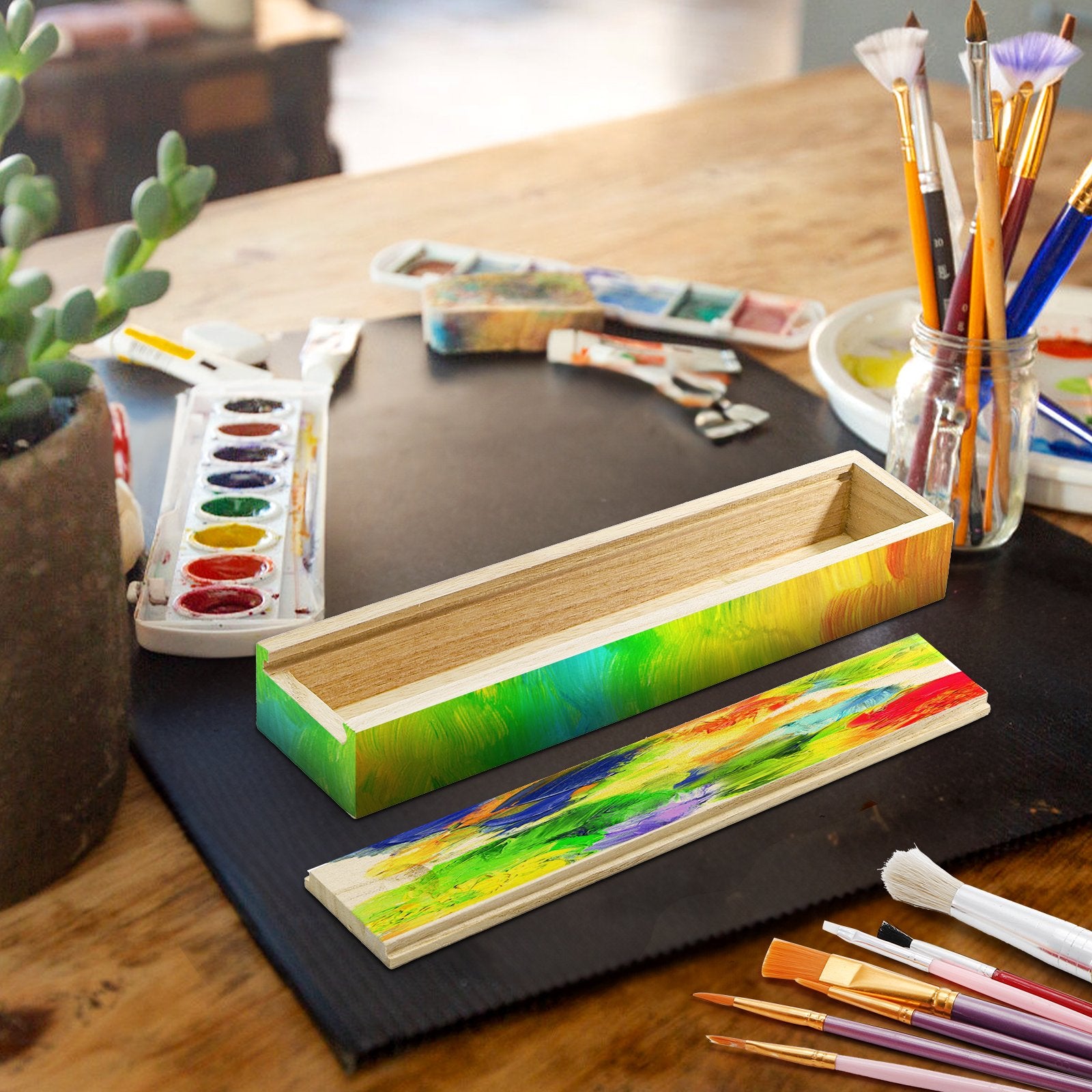 Unfinished pine wood box with sliding lid, decorated with colorful abstract brushstrokes, on a table with art supplies.
