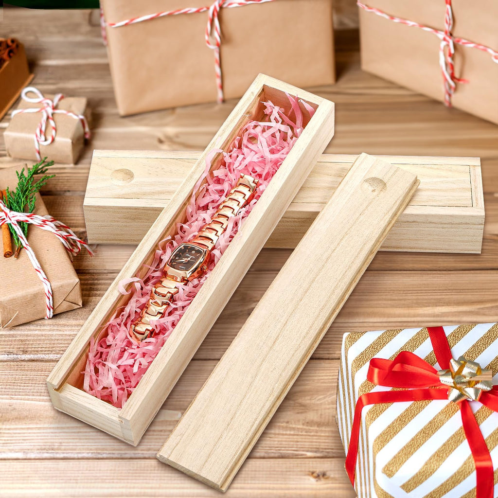 Unfinished pine wood box with sliding lid, open, showing pink shredded paper and a gold watch inside, with gift-wrapped boxes in the background.
