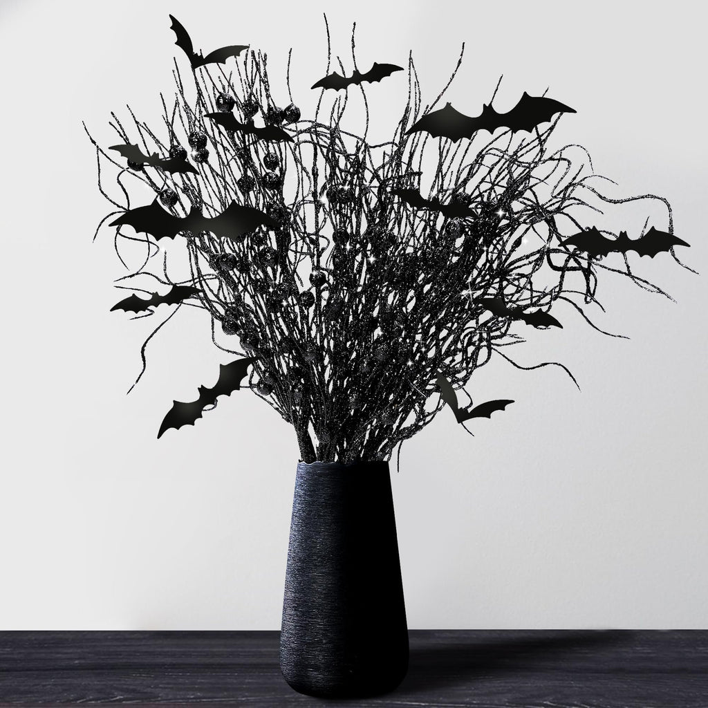 Black artificial Halloween branches with glitter and black bat cutouts in a black vase on a dark wooden surface.