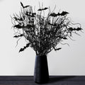 Black artificial Halloween branches with glitter and black bat cutouts in a black vase on a dark wooden surface.