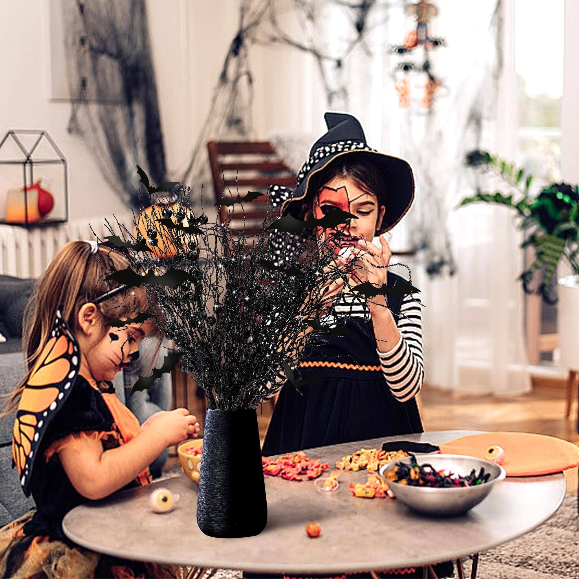 Two children in Halloween costumes decorating a table with artificial black branches adorned with bats.