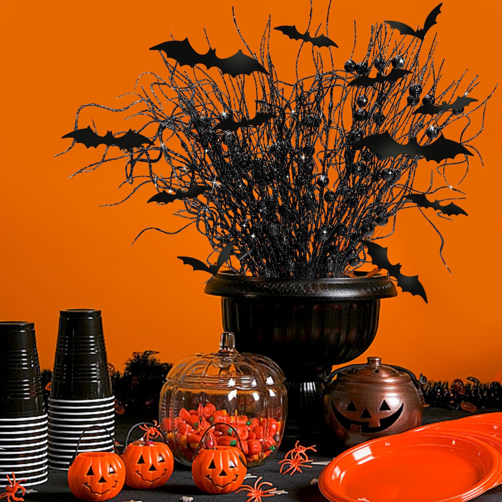 Halloween party table setting with black glitter branches adorned with bats, candy corn in a pumpkin jar, and orange plates.