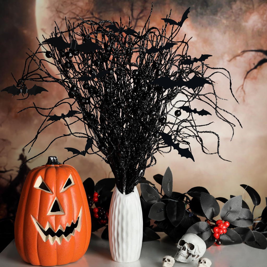 Halloween arrangement with a jack-o'-lantern, black glittery branches with bats, and skulls on a table with a moonlit background.