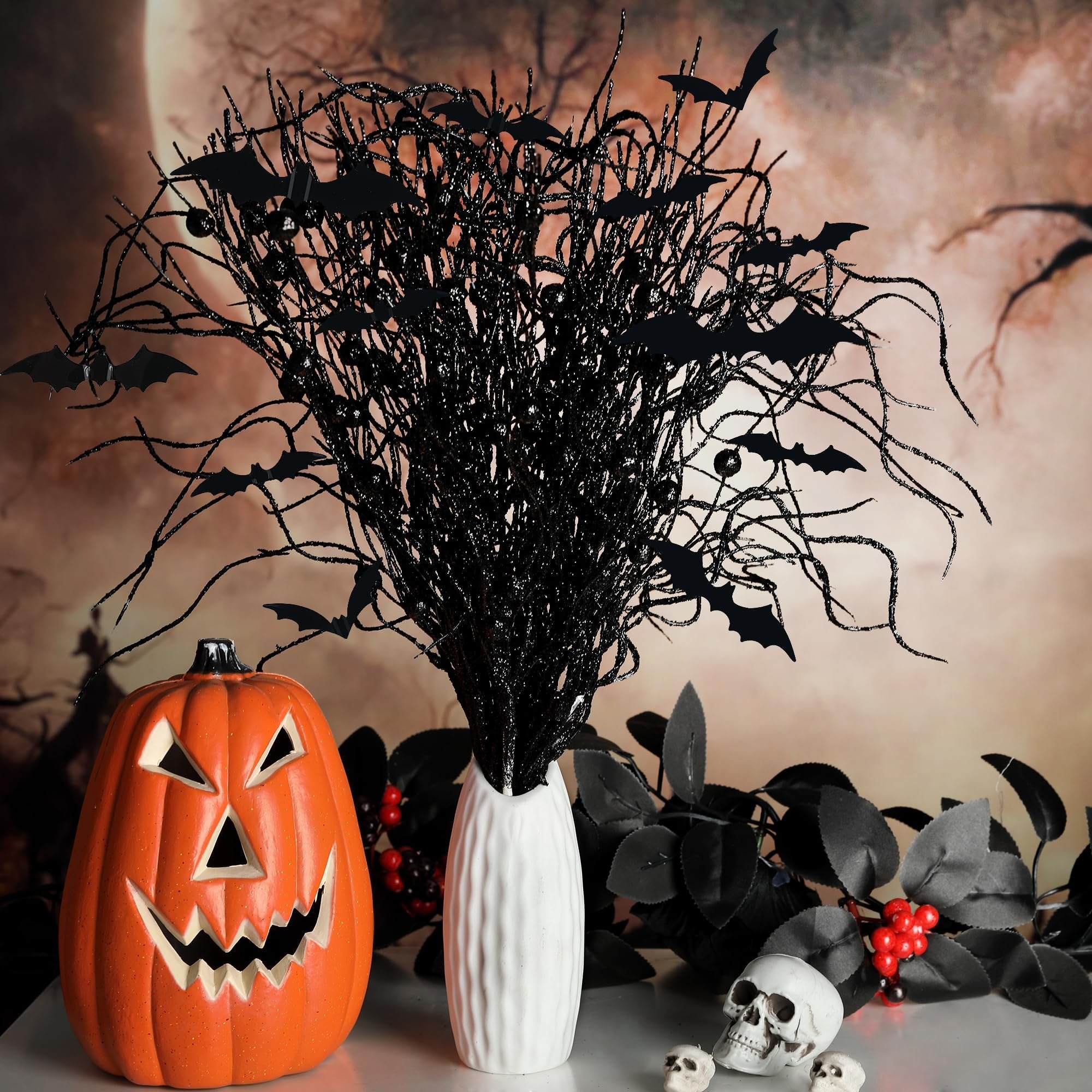 Halloween arrangement with a jack-o'-lantern, black glittery branches with bats, and skulls on a table with a moonlit background.