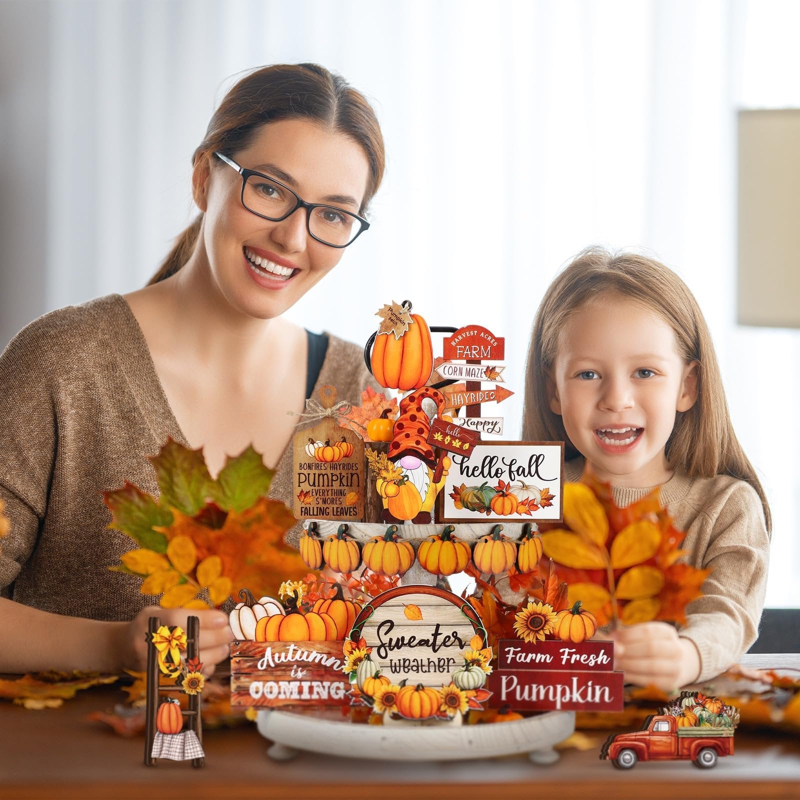 Woman and child smiling behind a tiered tray decor with fall-themed signs and pumpkins.