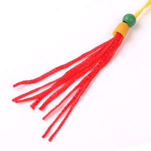 Close-up of red tassel with green bead and yellow plastic bead on white background