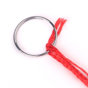Close-up of a silver metal ring with red string attached, isolated on a white background.