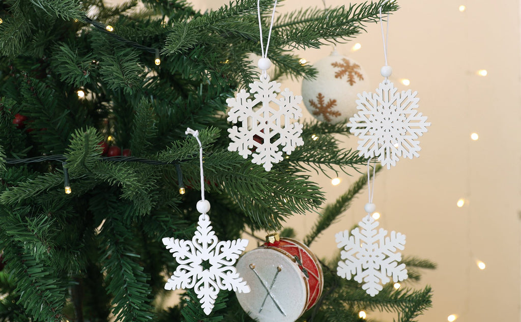 White wooden snowflake ornaments hanging on a Christmas tree with lights and a drum ornament.