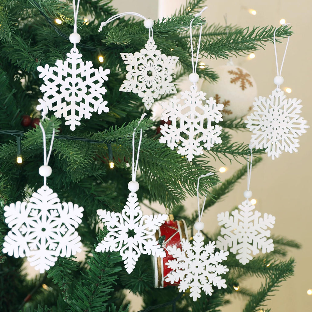 White wooden snowflake ornaments with white beads hanging on a Christmas tree with lights.