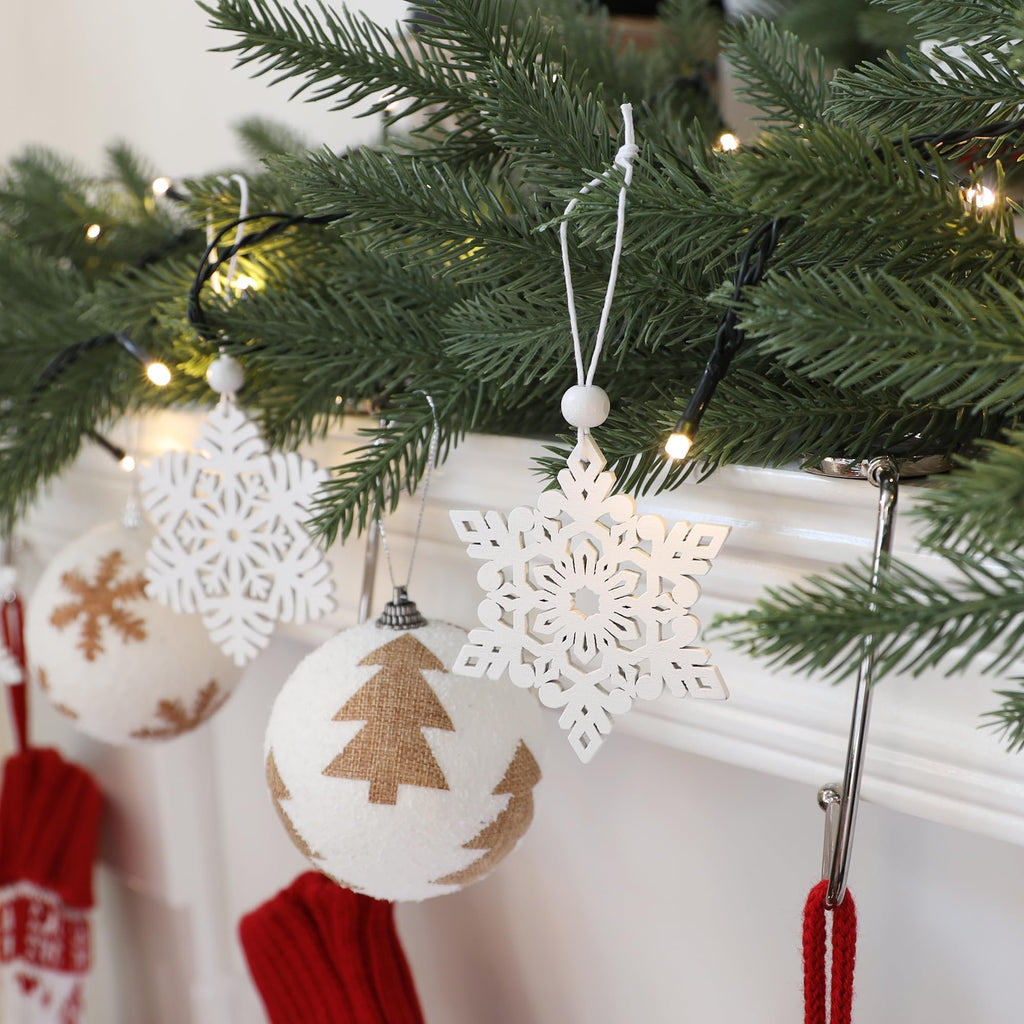 White wooden snowflake ornaments and textured Christmas balls hang from a decorated evergreen branch with lights.