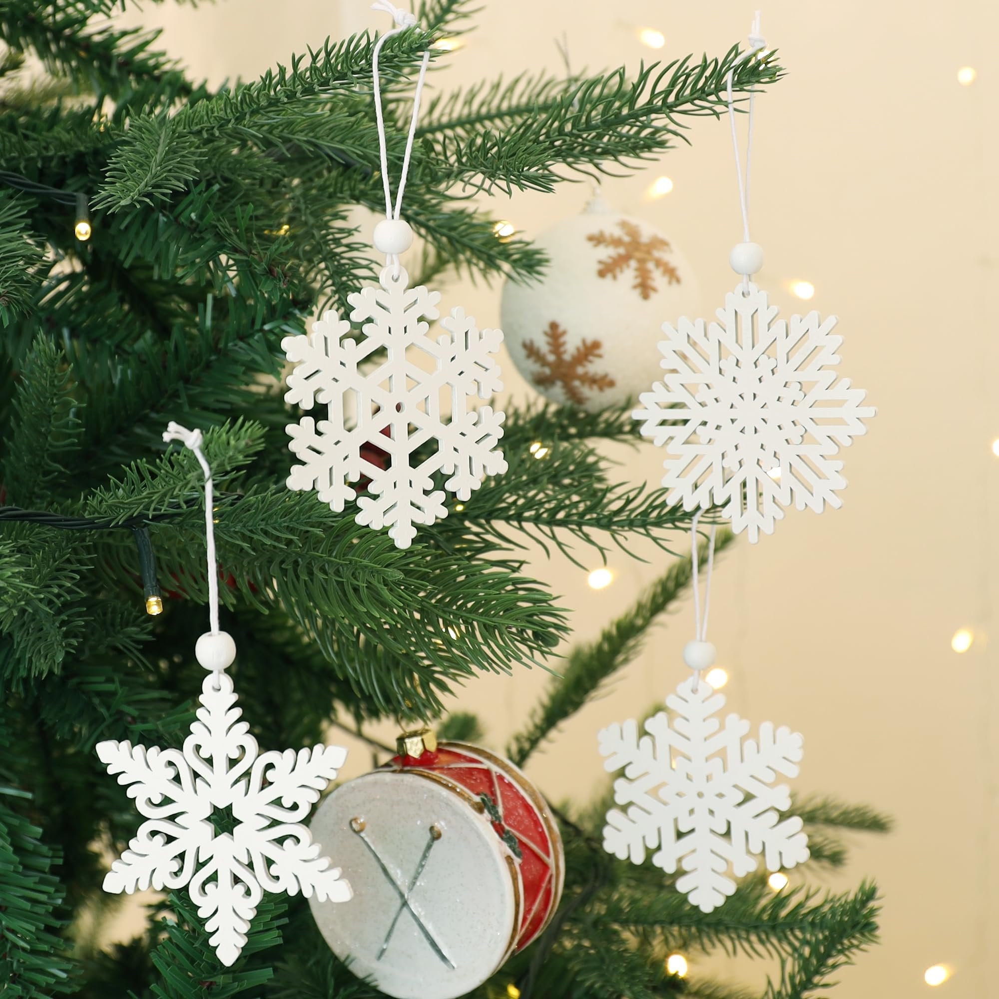 White wooden snowflake ornaments hanging on a Christmas tree with lights and a drum ornament.