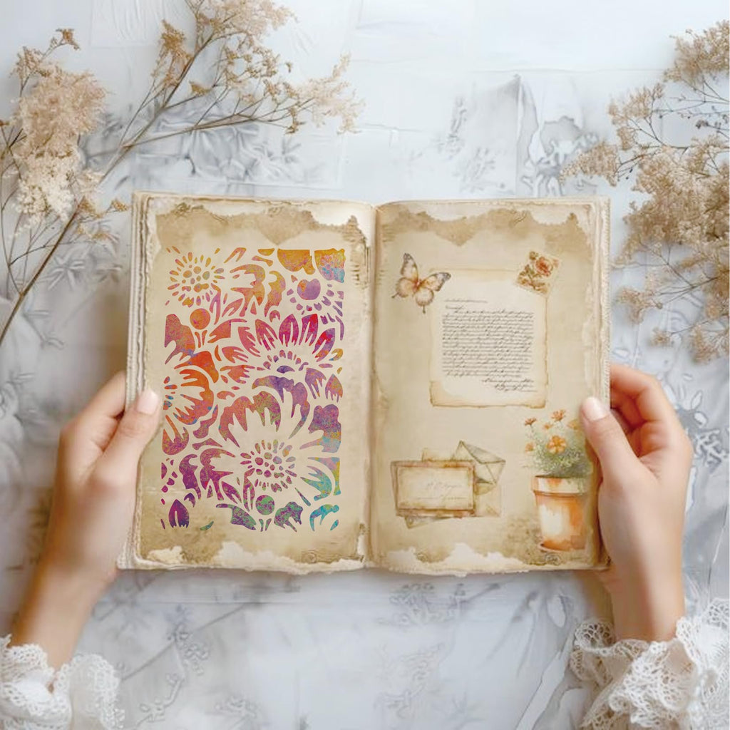 Hands holding open a vintage-style book with a floral stencil on the left page and decorative elements on the right.