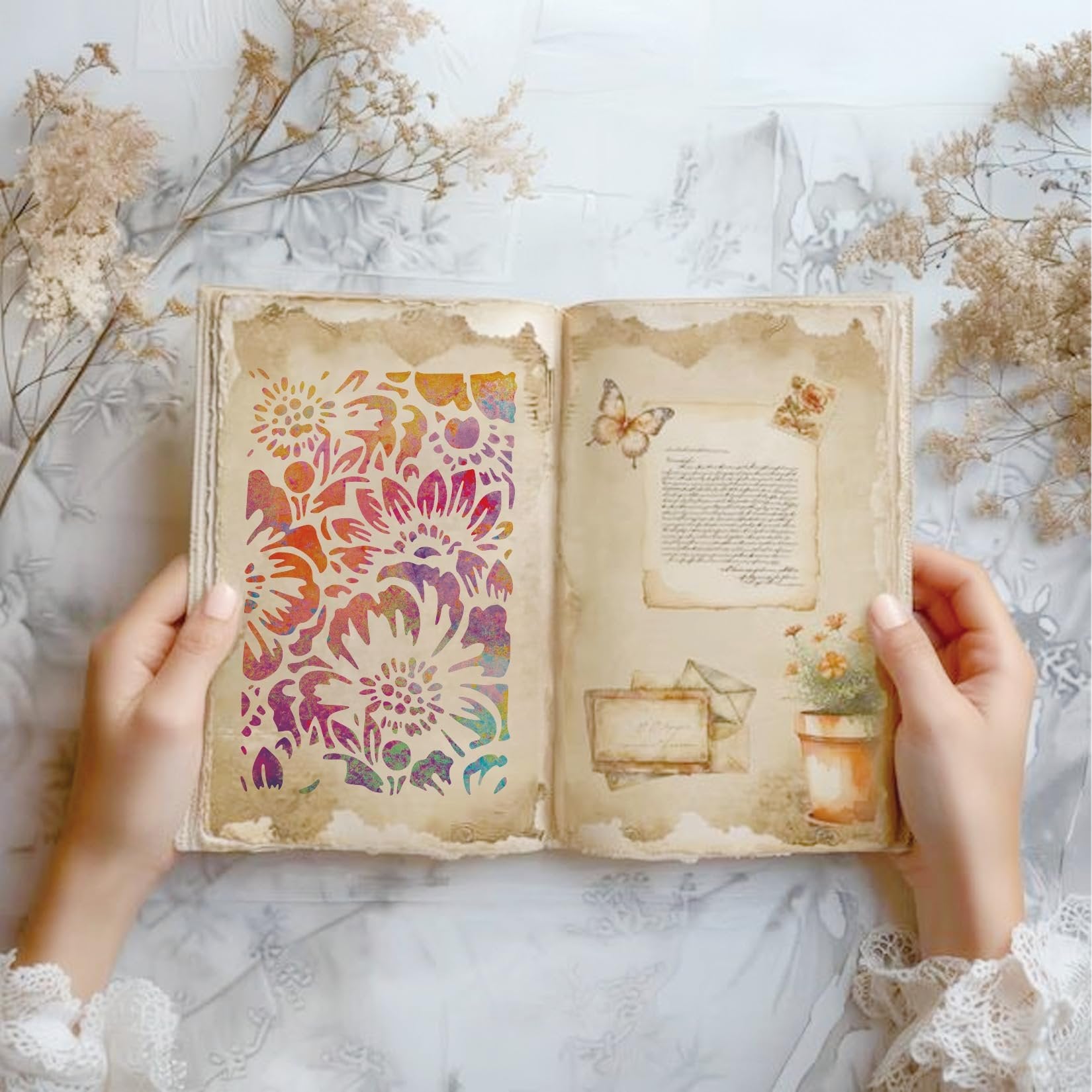 Hands holding open a vintage-style book with a floral stencil on the left page and decorative elements on the right.