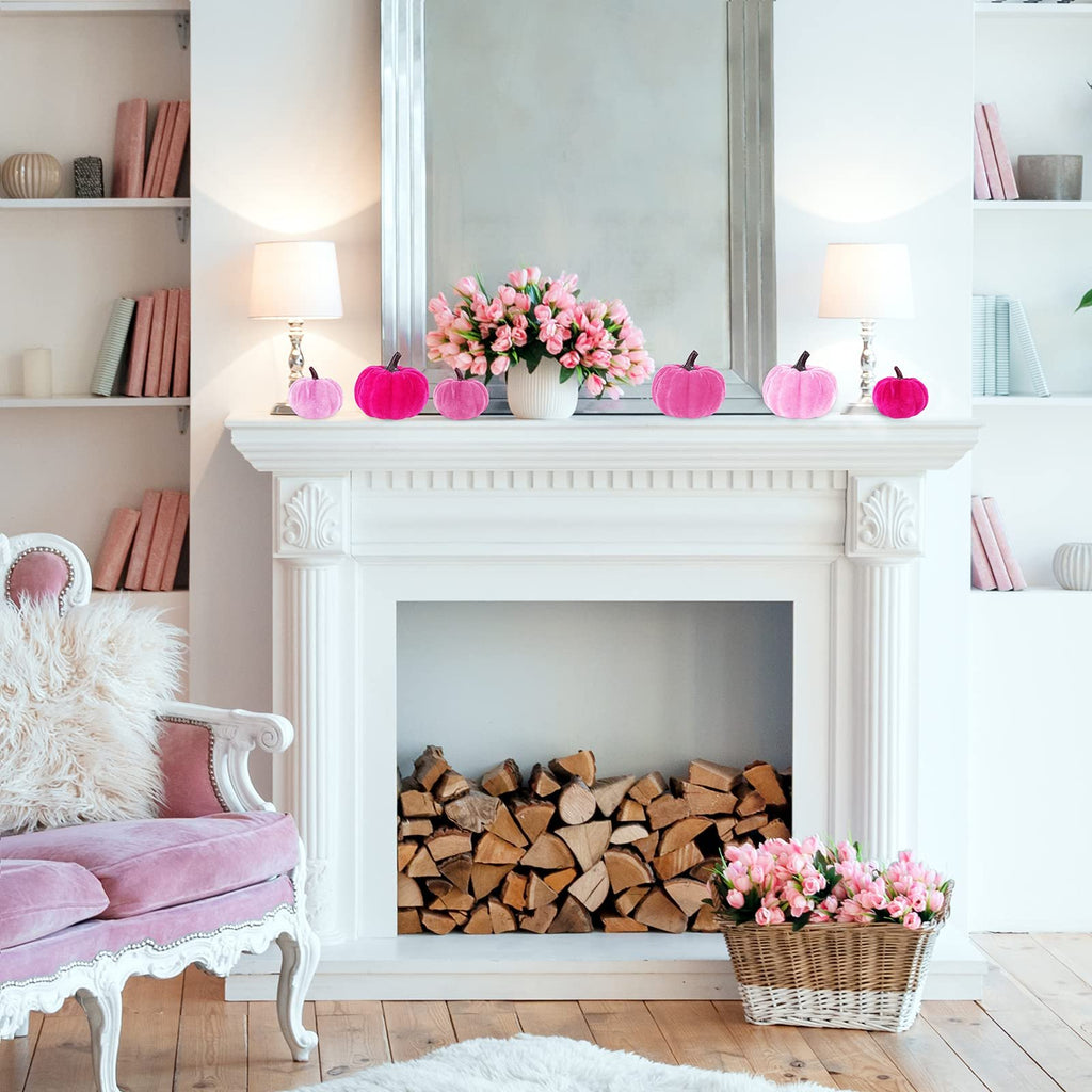 Assorted pink velvet pumpkins displayed on a white mantelpiece with a mirror and flowers