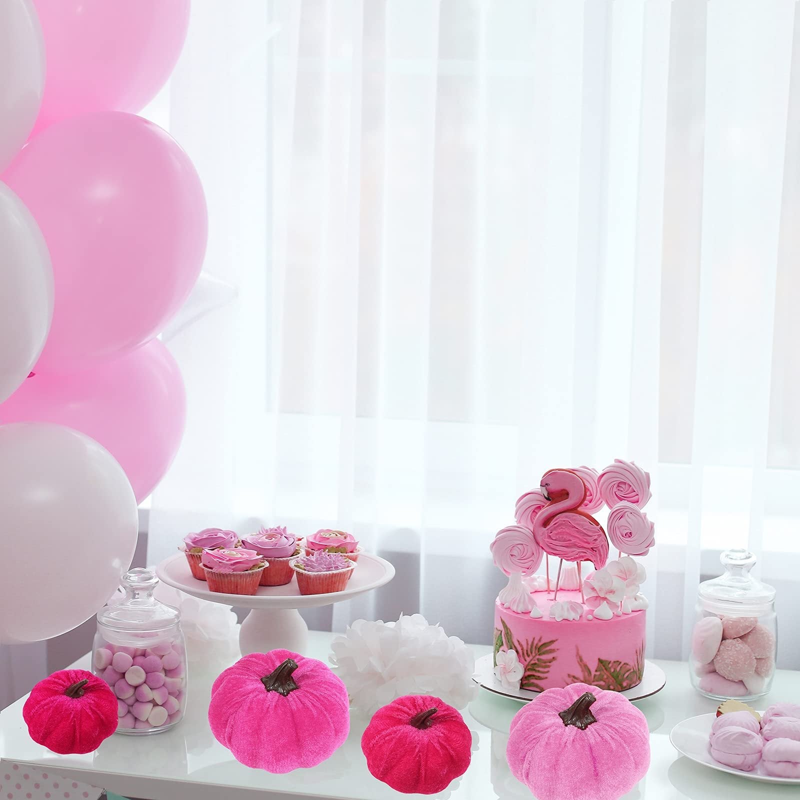 Assorted pink velvet pumpkins arranged on a table with a cake, cupcakes, and balloons for a party.