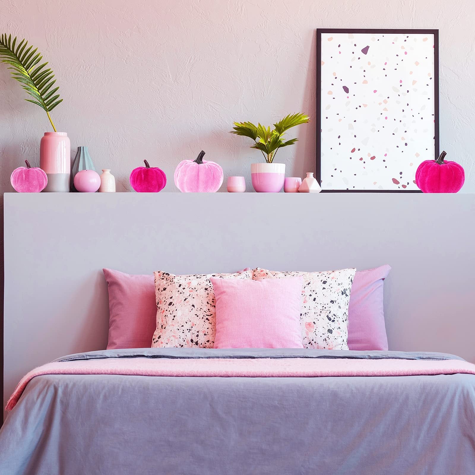Assorted pink velvet pumpkins displayed on a shelf above a bed with pink and gray bedding.