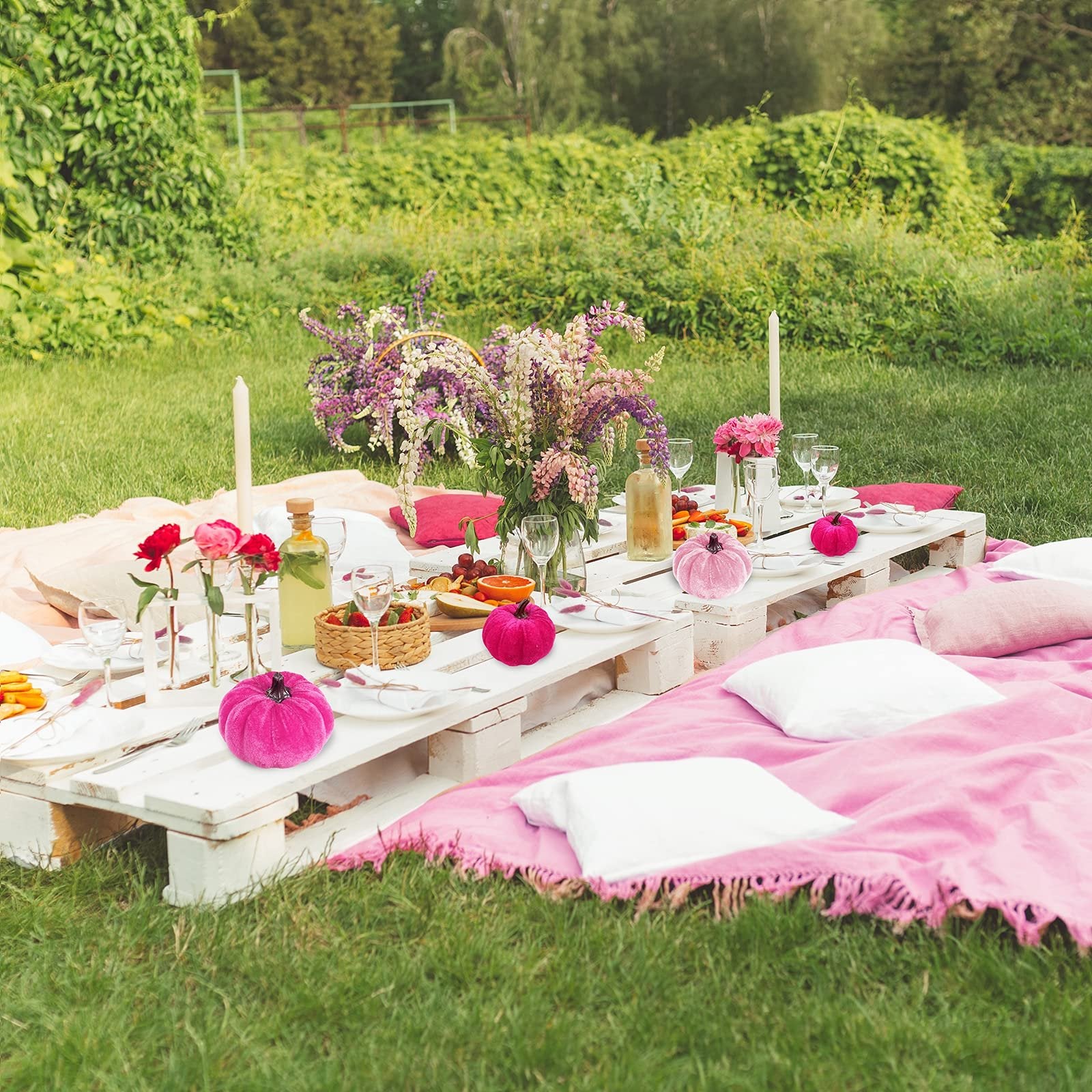Outdoor picnic table set with pink velvet pumpkins, flowers, and food on a sunny day.
