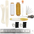 Bookbinding tools set including bone folder, creaser, needles, awl, thread, and clips on a ruler.
