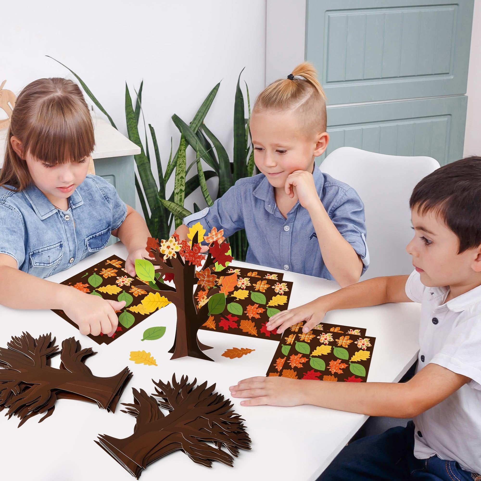 Three children crafting thankful trees with autumn leaf cutouts and tree trunk bases on a white table.