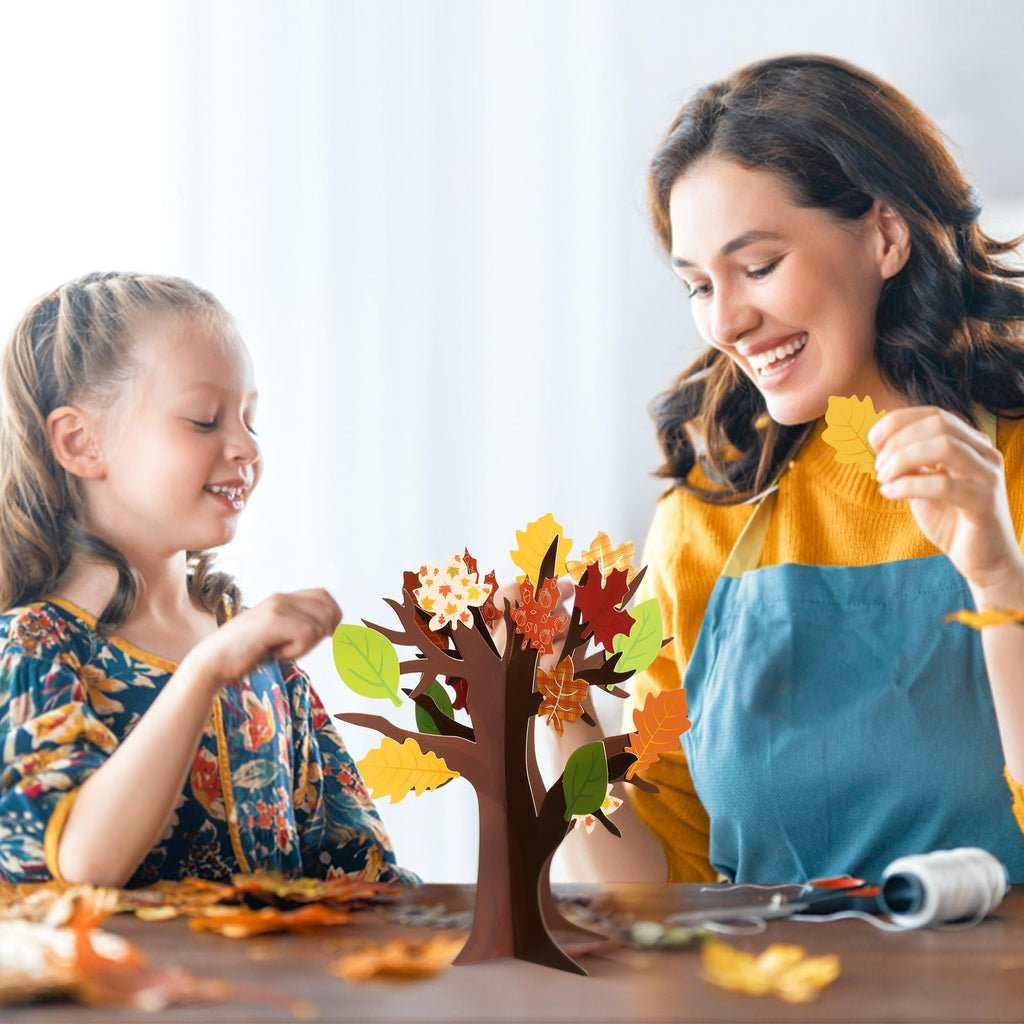 Mother and daughter crafting a fall tree with colorful leaf cutouts at a wooden table.