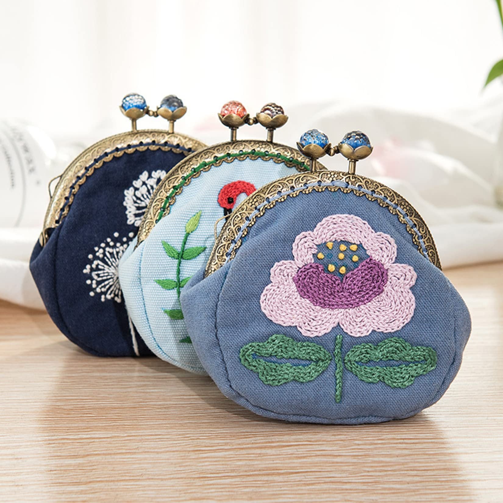 Three embroidered coin purses with metal clasps and decorative beads on a wooden surface.