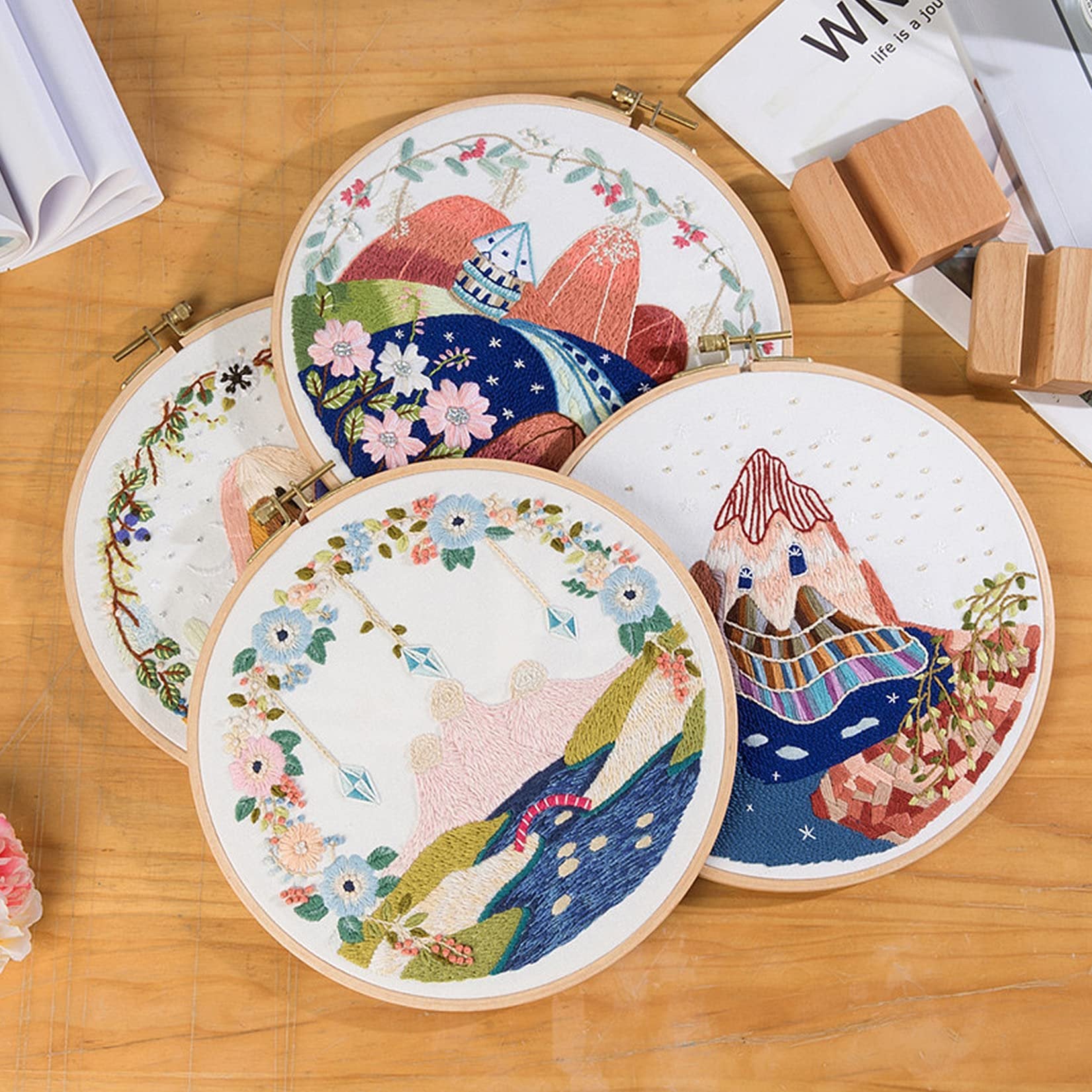 Four embroidered hoops with mountain and floral designs arranged on a wooden surface.