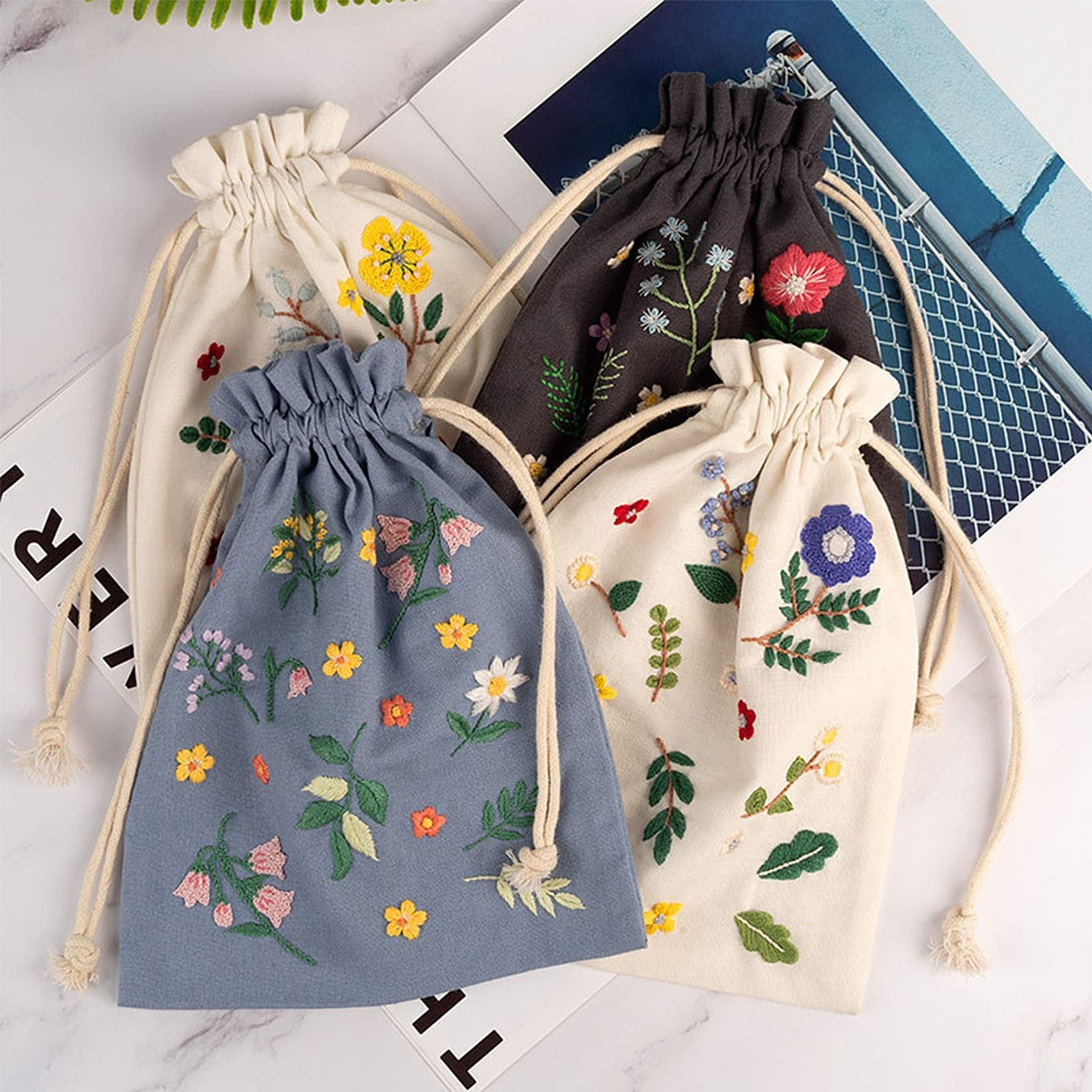 Four embroidered drawstring bags with floral patterns in cream, blue, and charcoal colors.