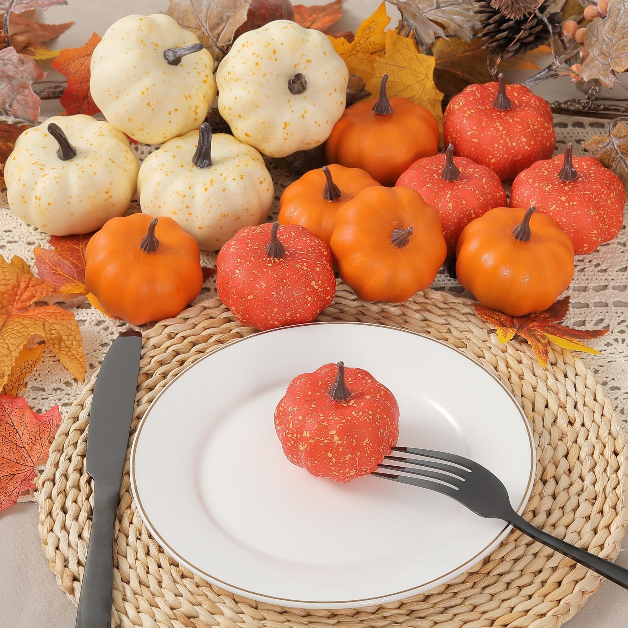 Miniature artificial pumpkins and fall leaves arranged on a table setting with a plate, fork, and knife.