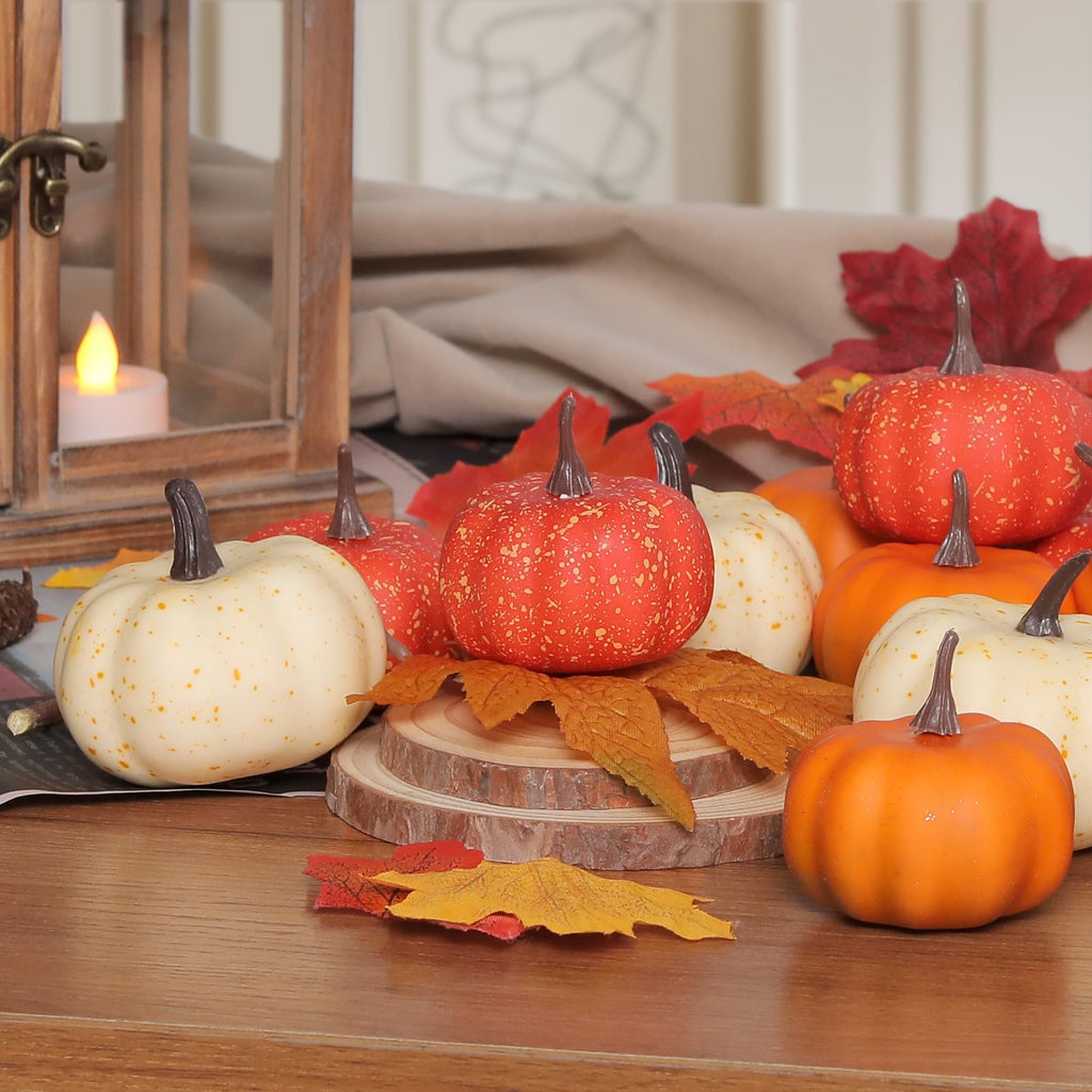 Assortment of artificial pumpkins and fall leaves arranged on a wooden surface with a lantern in the background.