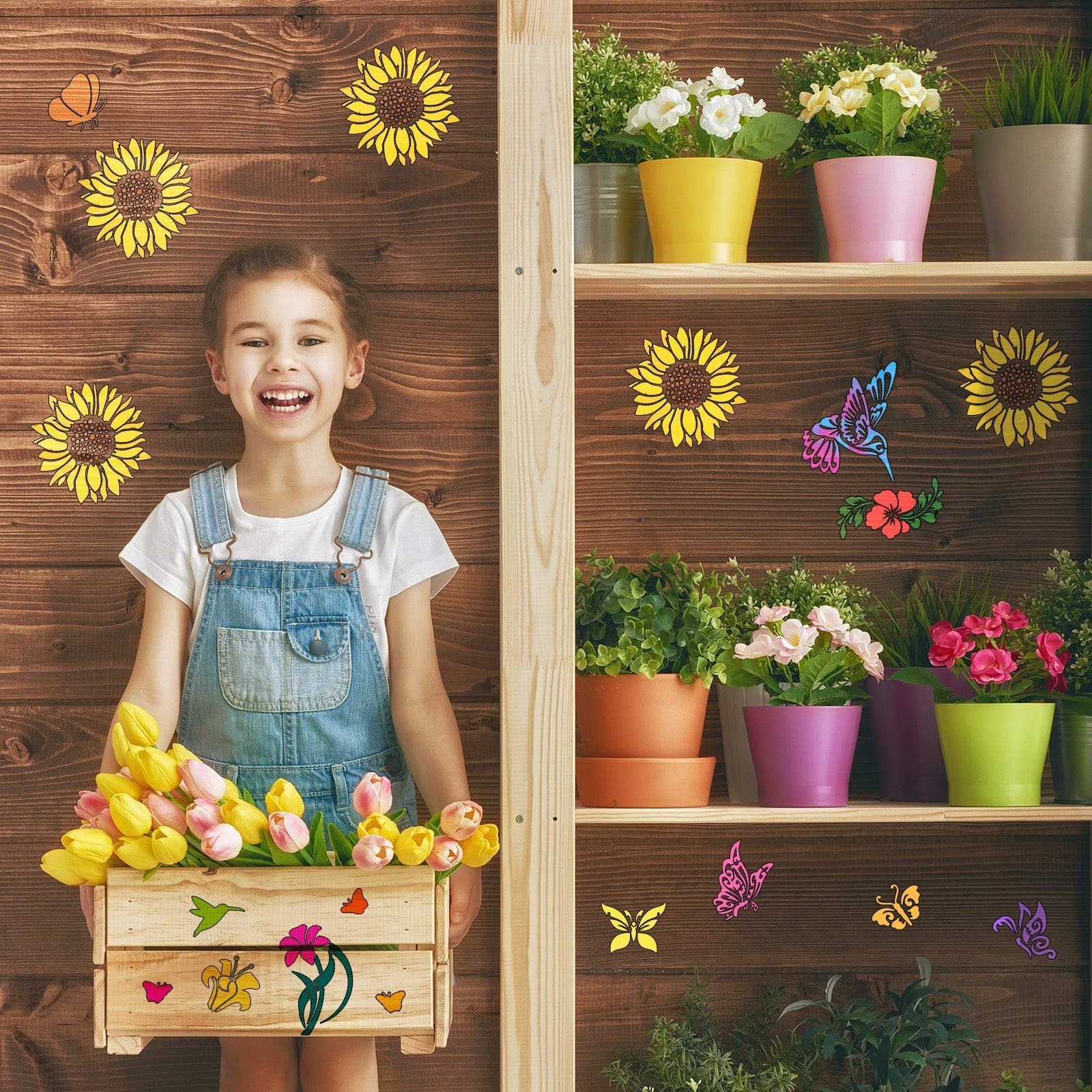 Smiling girl in denim overalls holding a wooden crate of tulips, with butterfly and sunflower stencils on a wooden wall and shelf.