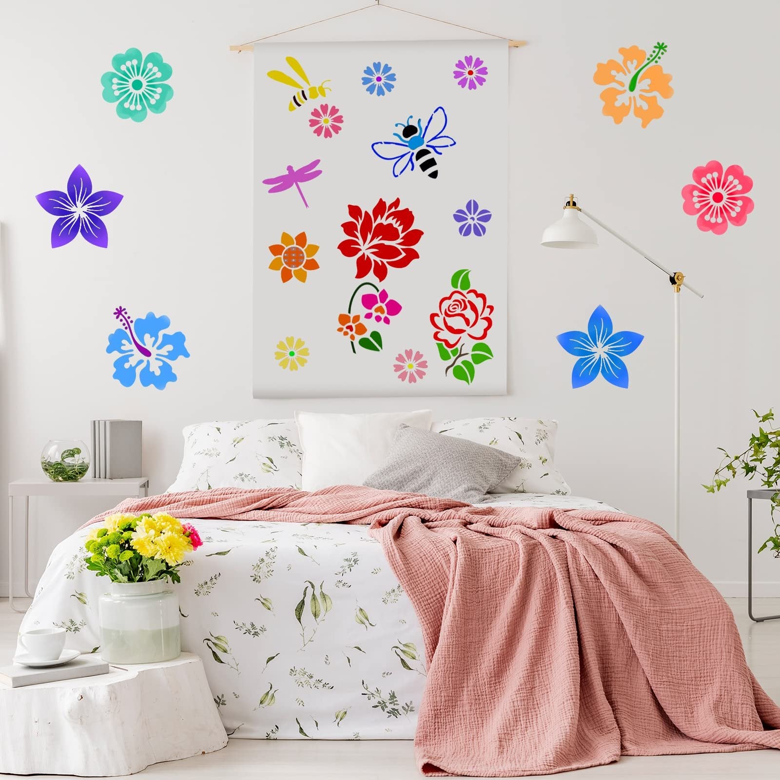 Bedroom scene with colorful flower and bee stencils applied to the wall above a bed with floral bedding and a pink throw blanket.