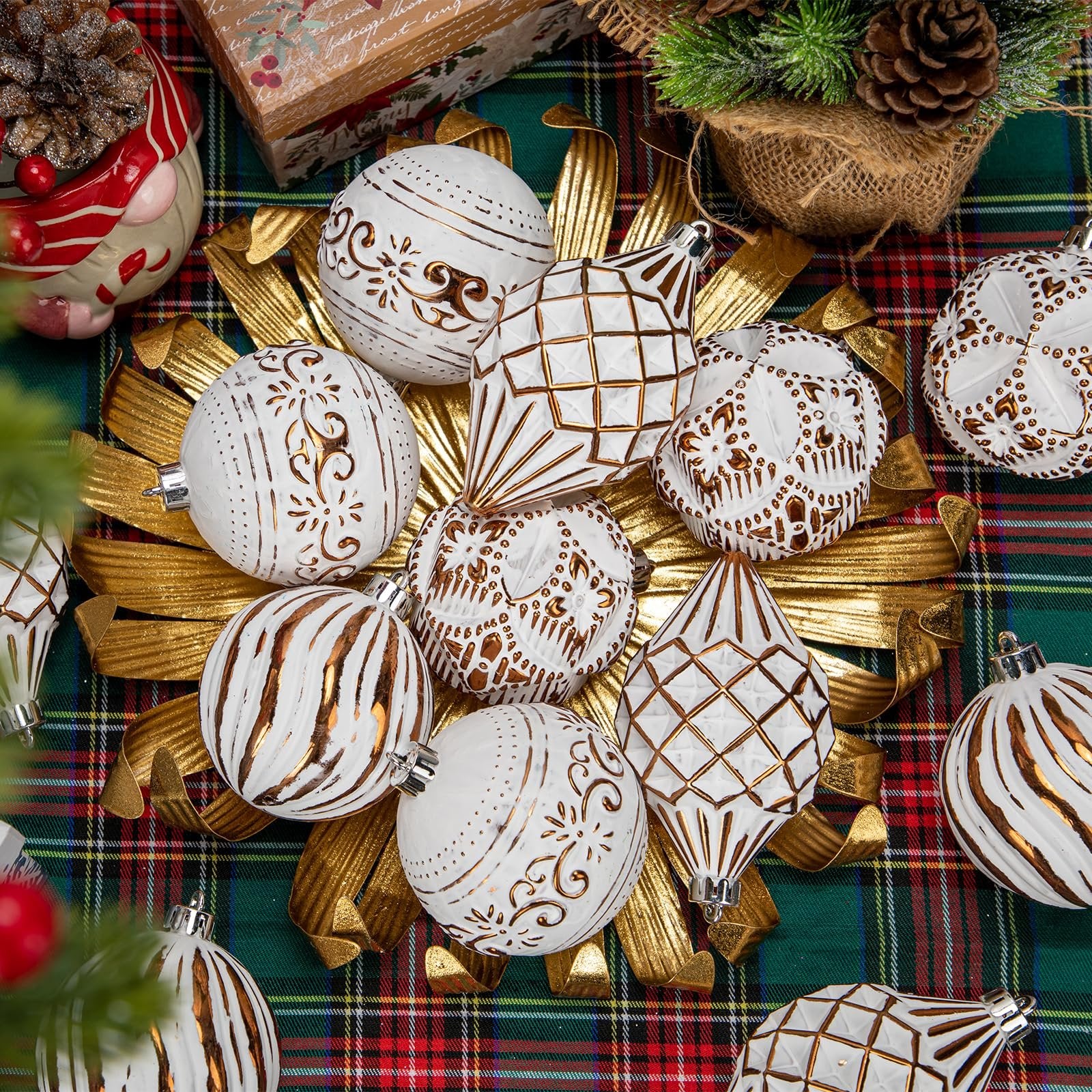 Assorted white and bronze hand-painted Christmas ball ornaments arranged on a gold decorative stand over a plaid tablecloth.