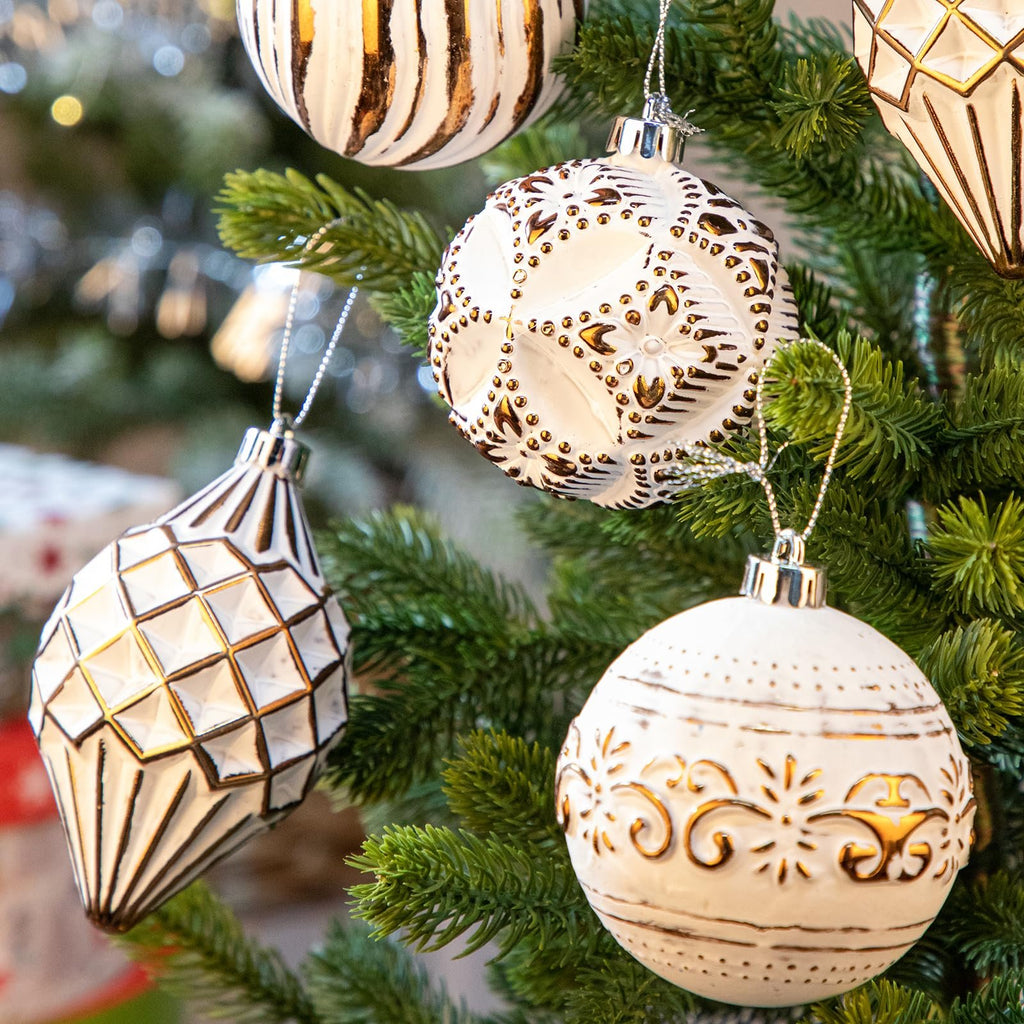 Assorted white and bronze hand-painted Christmas ball ornaments hanging on a green artificial Christmas tree.
