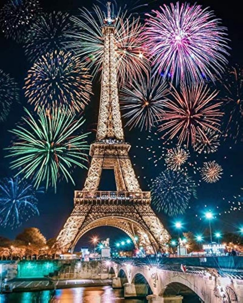 Eiffel Tower at night with fireworks exploding overhead, viewed from across a river with a bridge in the foreground.
