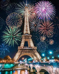 Eiffel Tower at night with fireworks exploding overhead, viewed from across a river with a bridge in the foreground.
