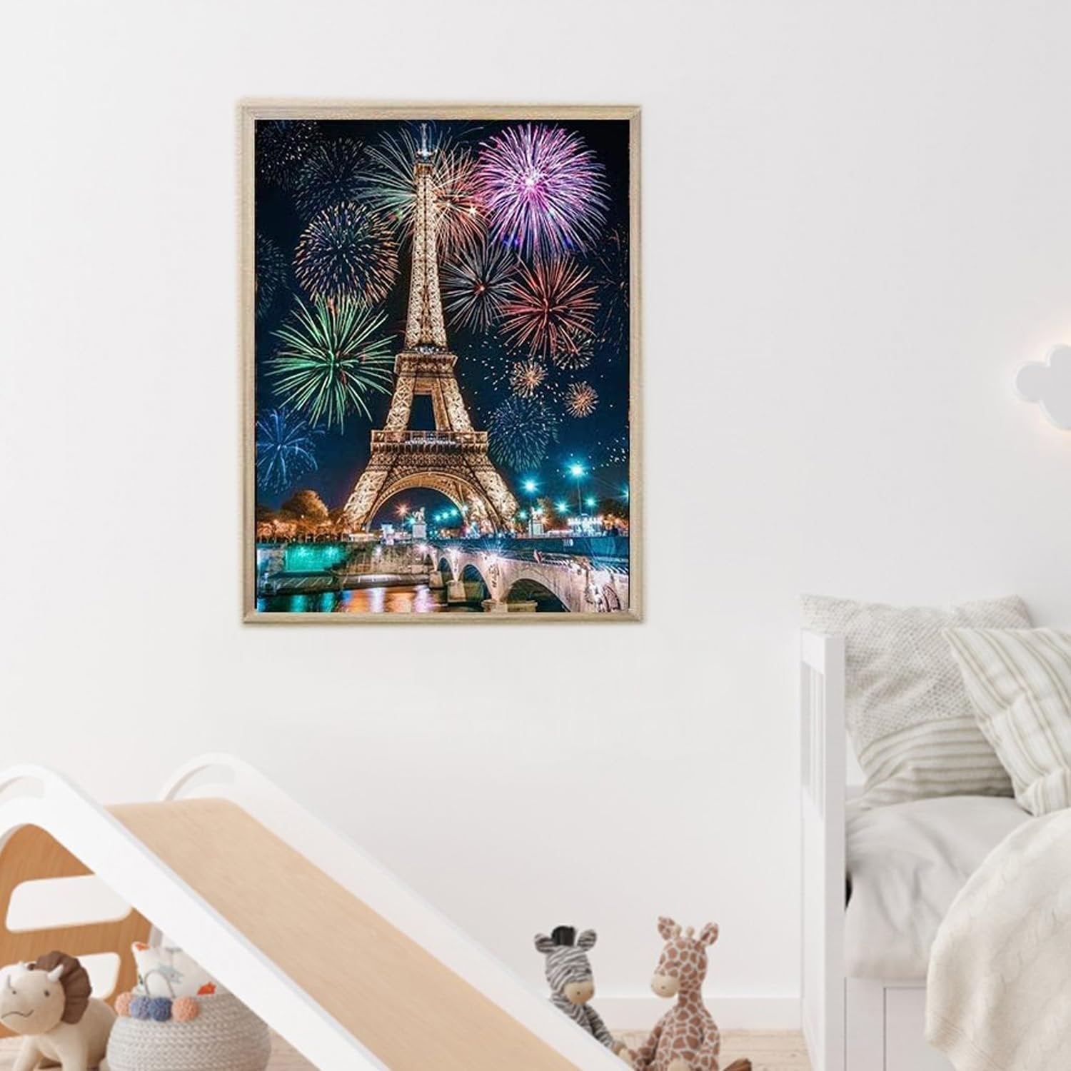 Diamond painting of the Eiffel Tower at night with fireworks, framed and hanging on a wall above a child's slide and bed.