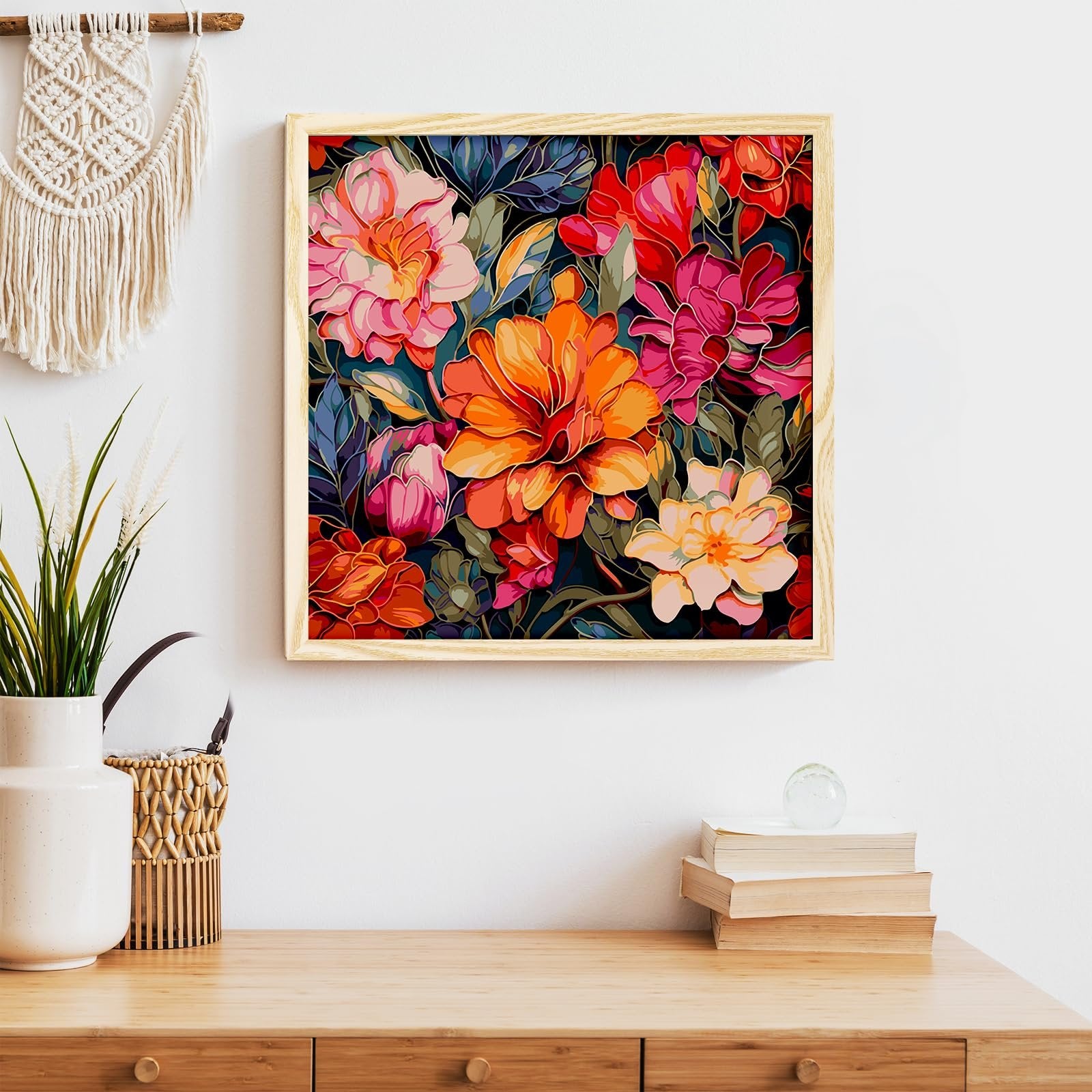 Framed floral paint by numbers artwork hanging on a white wall above a wooden desk with a vase and books.