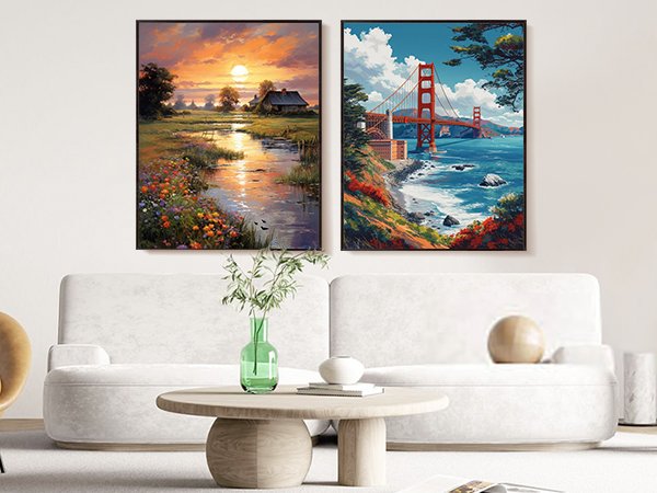 Two framed landscape paintings hanging above a sofa, one of a sunset over a rural stream and the other of the Golden Gate Bridge.