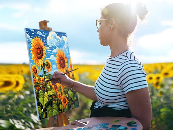 Woman painting sunflowers on canvas in a field, holding a palette and brush