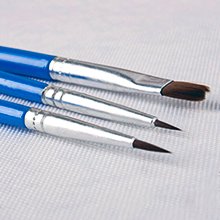 Three paint brushes with blue handles and silver ferrules on a textured white surface