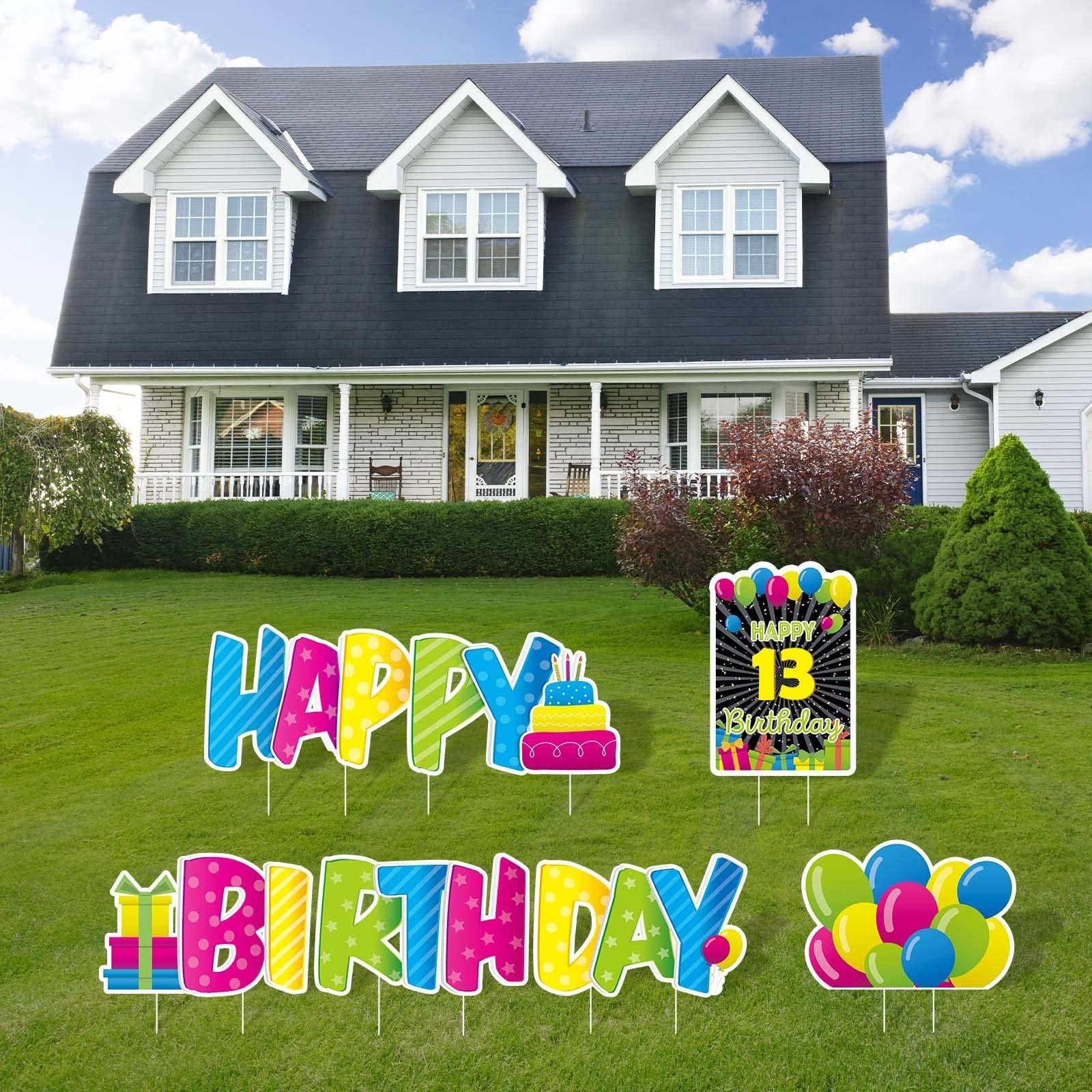 Colorful 'Happy Birthday' yard signs with stakes and a '13 Birthday' sign displayed on a green lawn in front of a house.
