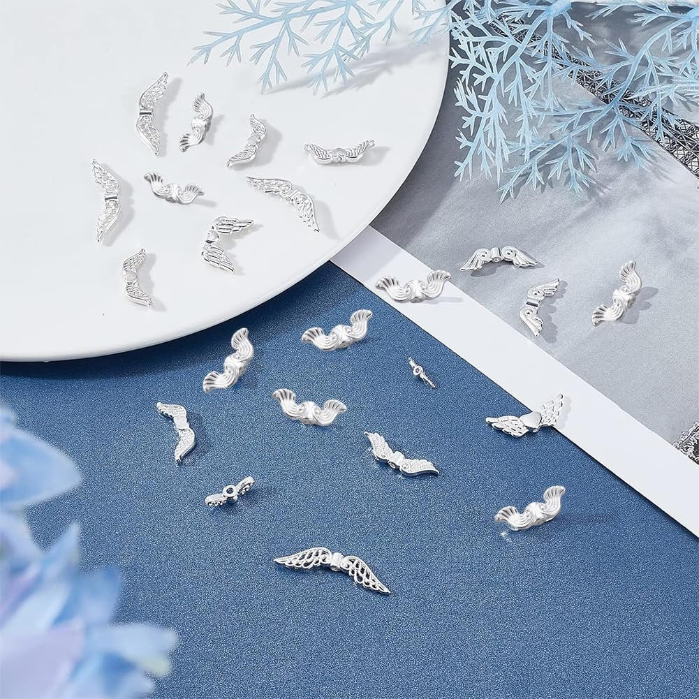 Assortment of silver-tone metal angel wing spacer beads scattered on a blue surface and a white plate.