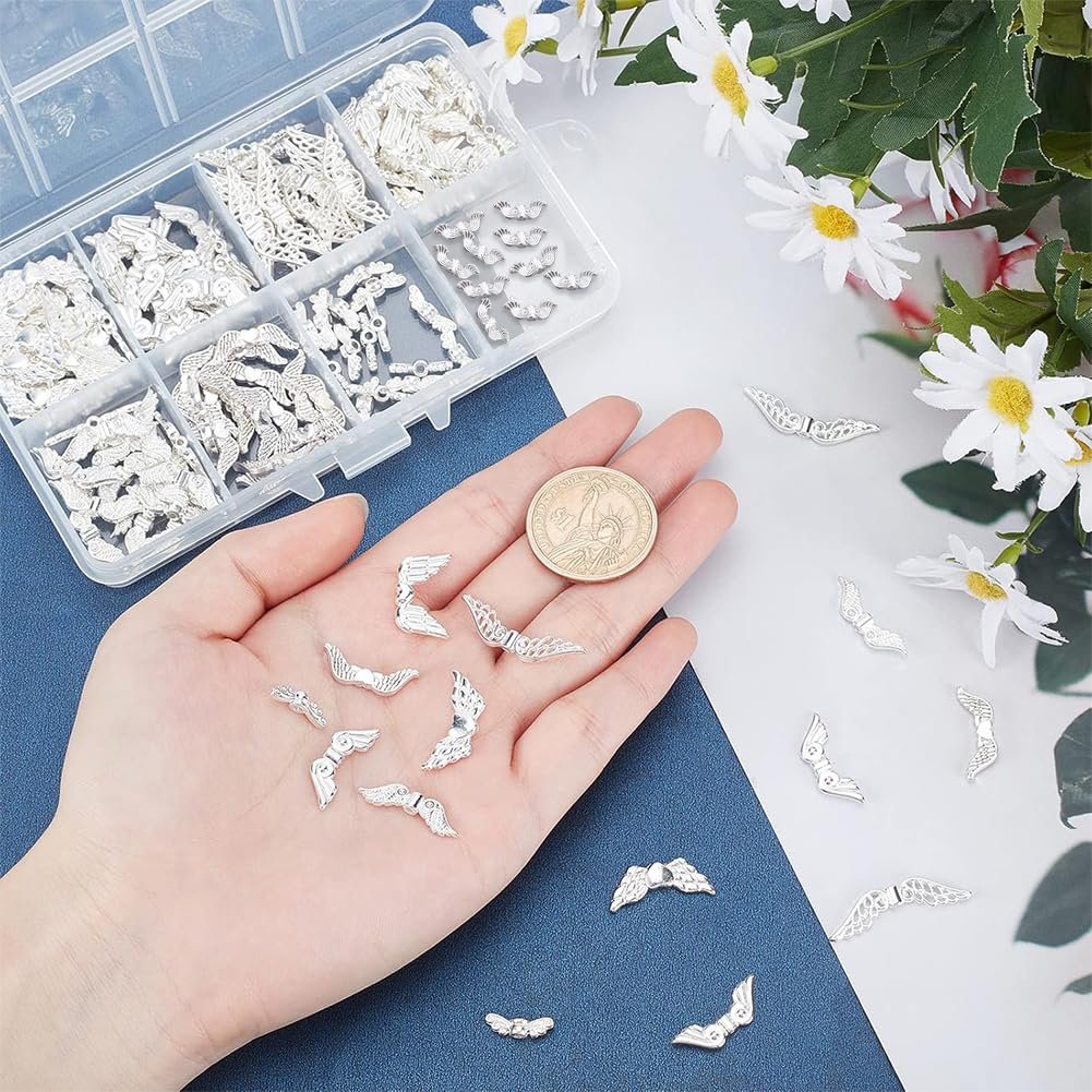 Hand holding assorted silver angel wing metal spacer beads next to a coin and a clear storage case filled with beads.